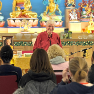 Kadam John teaching a group in the Heruka KMC meditation hall, with a Christmas garland and fairy lights along the front of the shrine