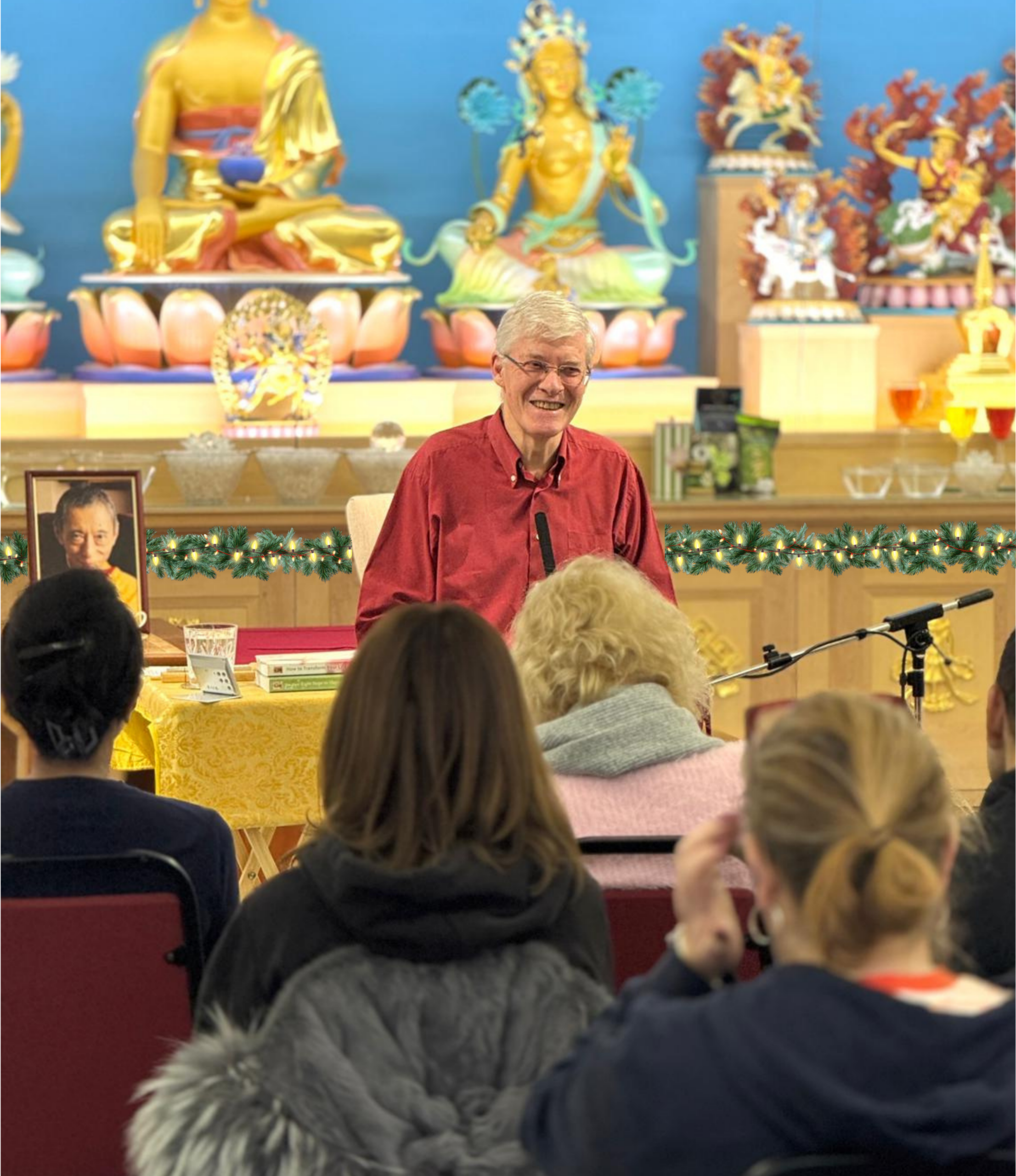Kadam John teaching a group in the Heruka KMC meditation hall, with a Christmas garland and fairy lights along the front of the shrine